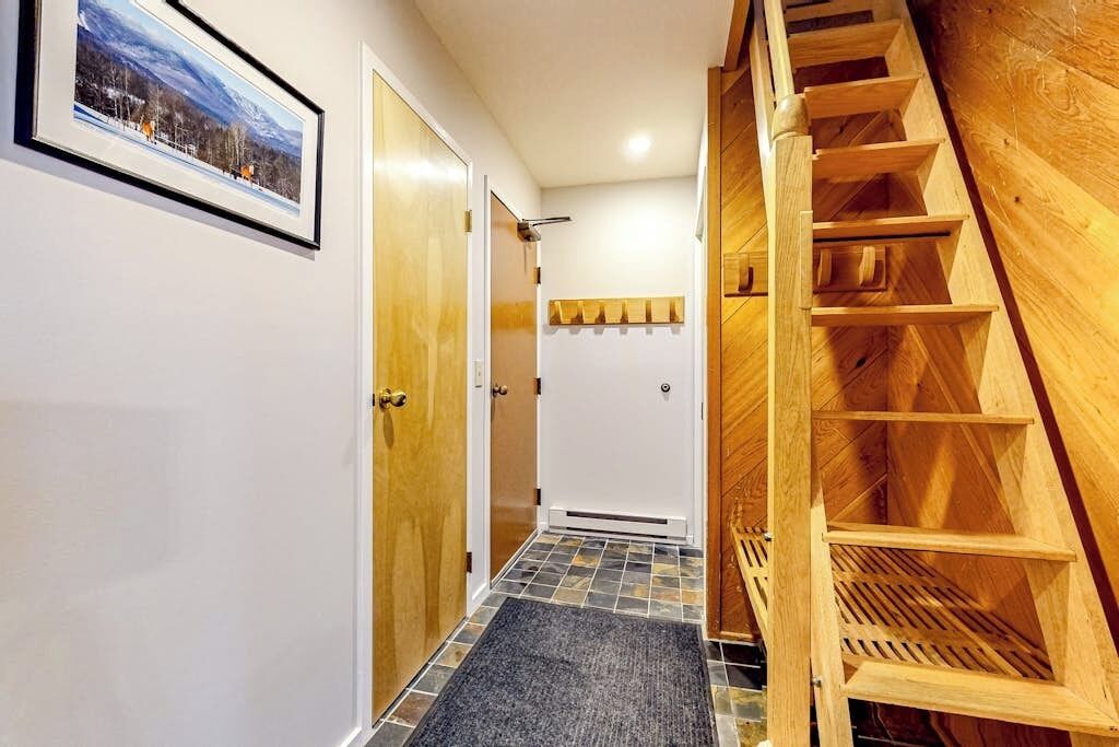 Un couloir avec un escalier en bois, une porte dotée d’une poignée et un tableau encadré accroché au mur.