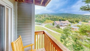Ein Balkon mit einem Holzstuhl, Blick auf eine Wohngegend mit Häusern und Bäumen, und ein bewölkter Himmel.