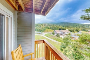 Ein Balkon mit einem Holzstuhl, Blick auf eine Wohngegend mit Häusern und Bäumen, und ein bewölkter Himmel.