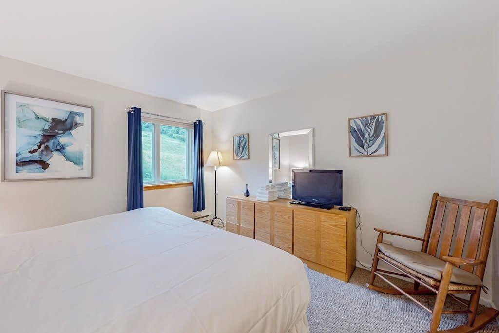 A hotel room with a large bed, a wooden dresser, a television, and artwork on the walls.