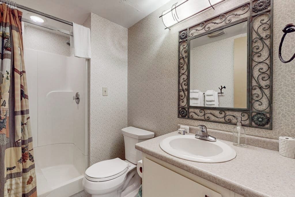 Une salle de bain équipée d’une douche, de toilettes, d’un lavabo et d’un miroir avec un cadre décoratif.