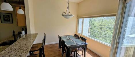 A dining area with a table and chairs, a kitchen counter, pendant lighting, and a large window with a view.