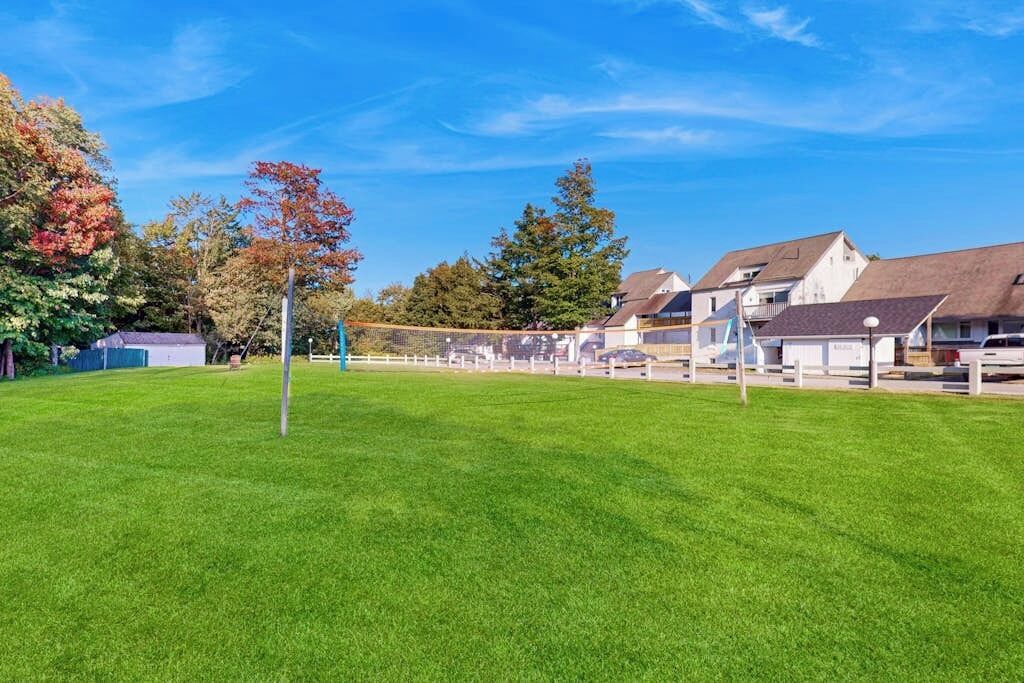 Ein grünes Feld mit einem Volleyballnetz, umgeben von Häusern mit schrägen Dächern.