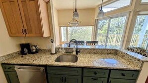 A kitchen with granite countertops, a stainless steel sink, green cabinets, and a window overlooking a deck. - Convenient Skier-friendly 1BR condo, pool, gym, tennis, fireplace, wifi (Warren)