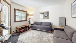 Ein Wohnzimmer mit grauem Sofa, einer Holzbank, einem kleinen Tisch, einer Lampe und einem Spiegel an der Wand.