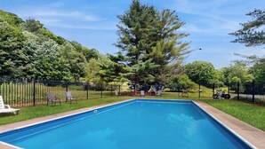 Ein rechteckiger Pool mit umgebendem Zaun, Bäumen und Liegestühlen.