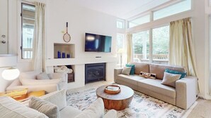 Una sala de estar moderna con sofá, mesa de centro, televisor, chimenea y ventanas amplias.