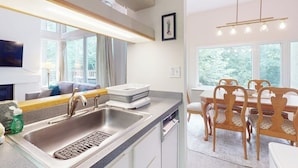 Una cocina moderna con un lavamanos, una zona de comedor con sillas de madera y ventanas amplias.