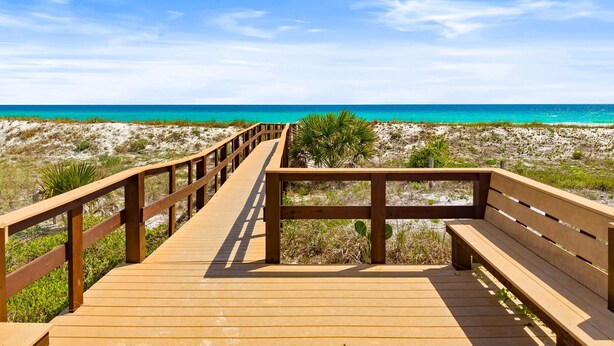 Una passerella di legno conduce a una spiaggia con acqua cristallina color turchese.