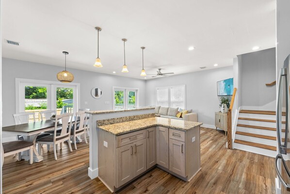 A modern kitchen with granite countertops, wooden cabinets, and a dining area with a table and chairs. - Brand new home! PCB West w/Pool, sleeps 10 (Panama City Beach)