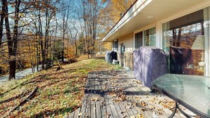 Et hus med en overdækket veranda, et vindue med udsigt til træer, og et udendørs bord med tag.