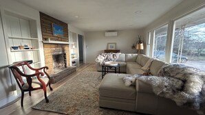 Un salon avec une cheminée, un canapé, un fauteuil et une vue sur l’extérieur.
