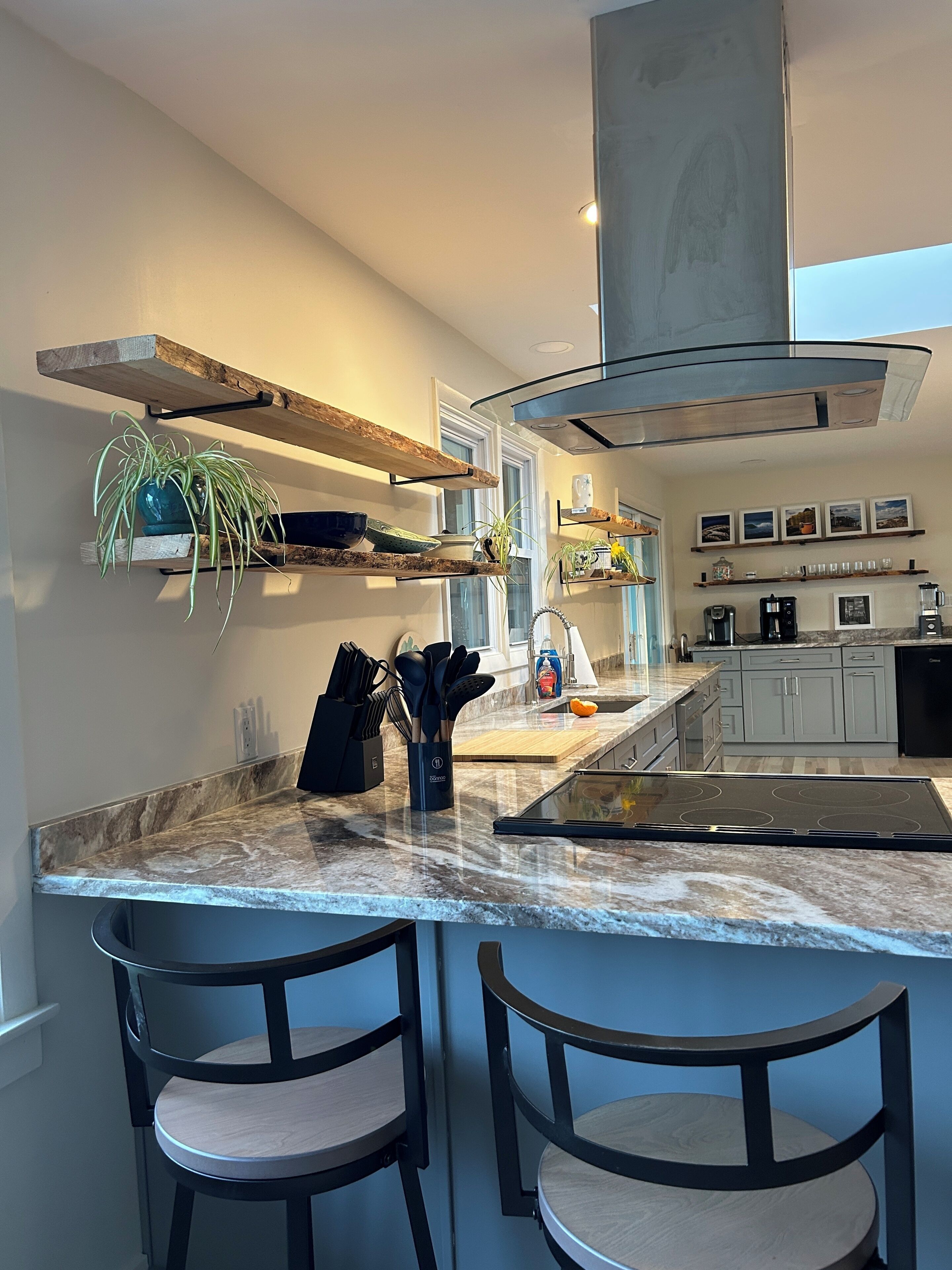 A modern kitchen with a central island, bar stools, and built-in shelves.