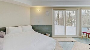 A bedroom with a large bed, a sliding glass door leading to a snowy outdoor area, and a small red chair. - Convenient townhouse w/ seasonal mountain views, pool, tennis, w/d, a/c, wifi (Warren)