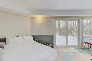 A bedroom with a large bed, a sliding glass door leading to a snowy outdoor area, and a small red chair. - Convenient townhouse w/ seasonal mountain views, pool, tennis, w/d, a/c, wifi (Warren)