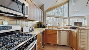 A modern kitchen with a gas stove, microwave, and built-in oven. There is a large window providing natural light and a view of the outdoors. - Convenient townhouse w/ seasonal mountain views, pool, tennis, w/d, a/c, wifi (Warren)