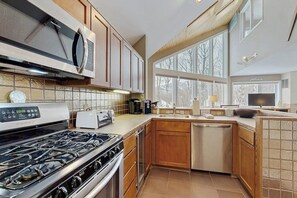 A modern kitchen with a gas stove, microwave, and built-in oven. There is a large window providing natural light and a view of the outdoors. - Convenient townhouse w/ seasonal mountain views, pool, tennis, w/d, a/c, wifi (Warren)