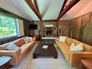 A cozy living room with two sofas, a coffee table, a fireplace, and a TV mounted on the wall. - Cozy house nestled in the woods w/ balcony, close to recreation, w/d, wifi, TV (Warren)