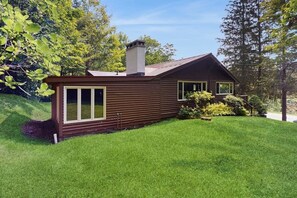 Een houten blokhut met twee verdiepingen, een schuin dak, een schoorsteen en een verzorgd gazon.