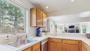 A modern kitchen with wooden cabinets, a built-in dishwasher, a large window, and a view of trees outside. - Home w/ mountain view, deck, shared pool & tennis, w/d (Warren)