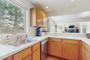 A modern kitchen with wooden cabinets, a built-in dishwasher, a large window, and a view of trees outside. - Home w/ mountain view, deck, shared pool & tennis, w/d (Warren)