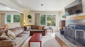 A living room with a sofa, a red coffee table, a fireplace, and a television mounted above it. - Home w/ mountain view, deck, shared pool & tennis, w/d (Warren)