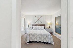Ein Schlafzimmer mit einem großen Bett, Nachttischen mit Lampen, einem Holzkopfende und einem großen Fenster.