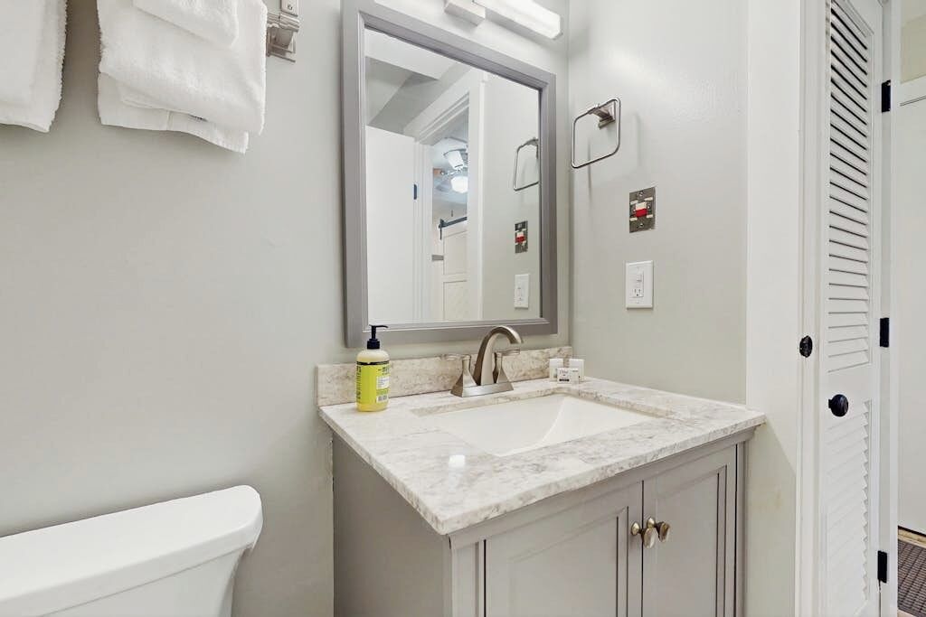 A bathroom with a white toilet, a sink with a marble countertop, a mirror, and a towel rack.