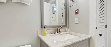 A bathroom with a white toilet, a sink with a marble countertop, a mirror, and a towel rack.