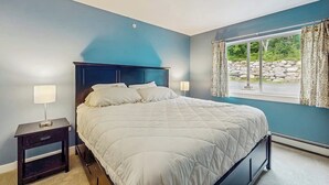 Ein Schlafzimmer mit einem Bett, Nachttischen und einem Fenster mit Vorhängen.