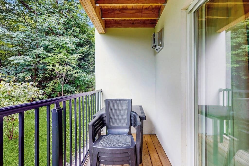 A balcony with a wooden ceiling, a black chair, and a glass door.