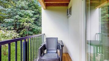 A balcony with a wooden ceiling, a black chair, and a glass door.