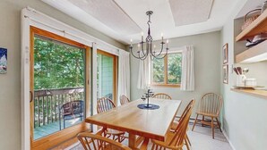 Un comedor con una mesa y sillas de madera, una araña y ventanas grandes con vistas a zonas verdes.