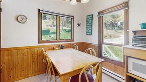 A dining area with a wooden table and chairs, a clock on the wall, and a window with a view of the outdoors.