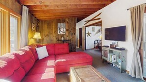 A cozy living room with a red sofa, wooden ceiling beams, a television, and a bookshelf.