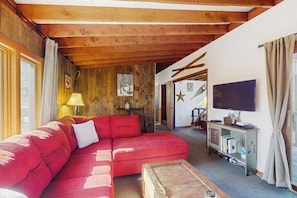 Ein gemütliches Wohnzimmer mit einem roten Sofa, Holzbalken an der Decke, einem Fernseher und einem Bücherregal.