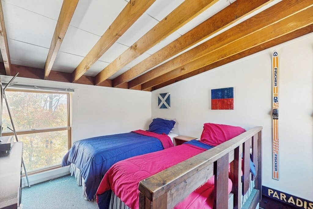 A room with two beds, wooden beams, a window, a ski pole, and a flag.