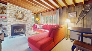 A cozy living room with a fireplace, red sofa, wooden beams, and a bookshelf.