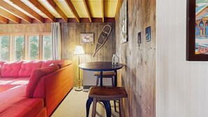 A cozy room with a wooden ceiling, a red sofa, a round table with a stool, and a poster on the wall.