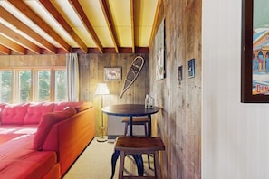 Ein gemütlicher Raum mit Holzbalkendecke, einem roten Sofa, einem runden Tisch mit Hocker und einem Poster an der Wand.