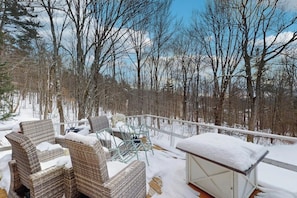 Une terrasse dotée de meubles en osier et d’une table en verre, entourée d’un paysage enneigé et d’arbres.