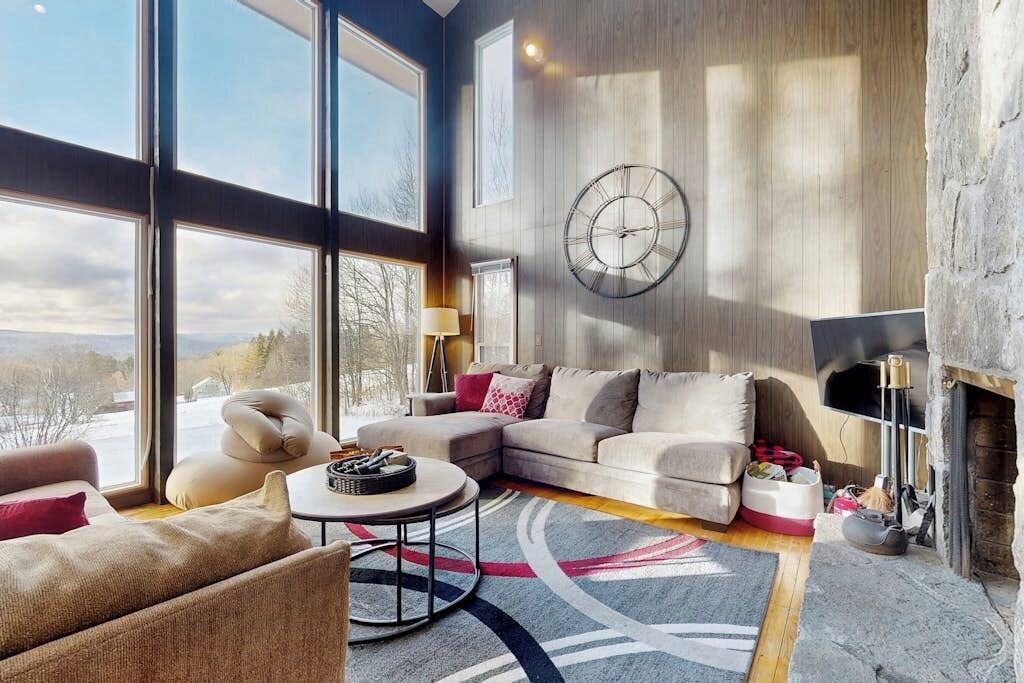 Un salon spacieux doté d’une grande fenêtre, d’une cheminée et d’une horloge moderne accrochée au mur.