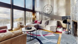Een ruime woonkamer met een groot raam, een open haard en een moderne klok aan de muur.