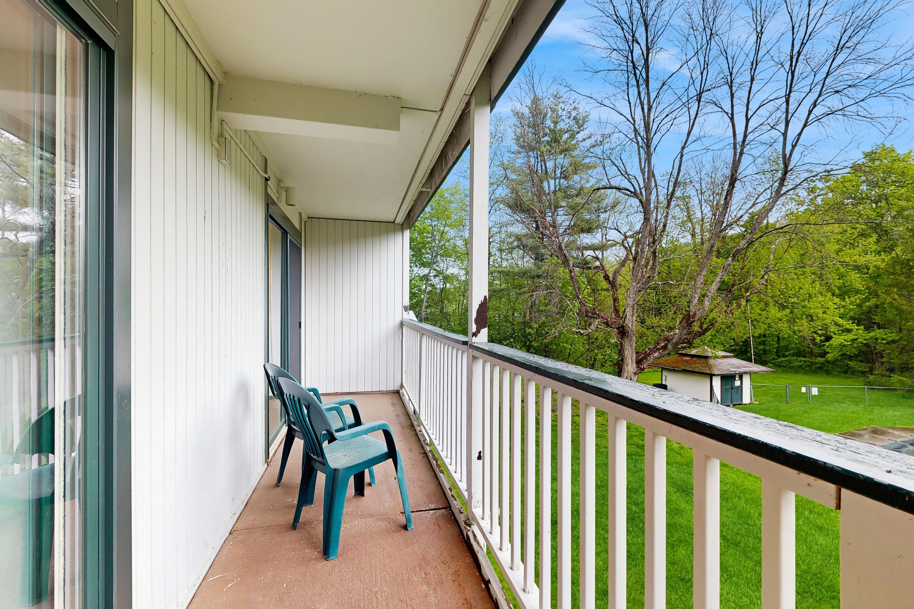 Un balcon avec deux chaises, une balustrade blanche et une vue sur une pelouse verdoyante et des arbres.