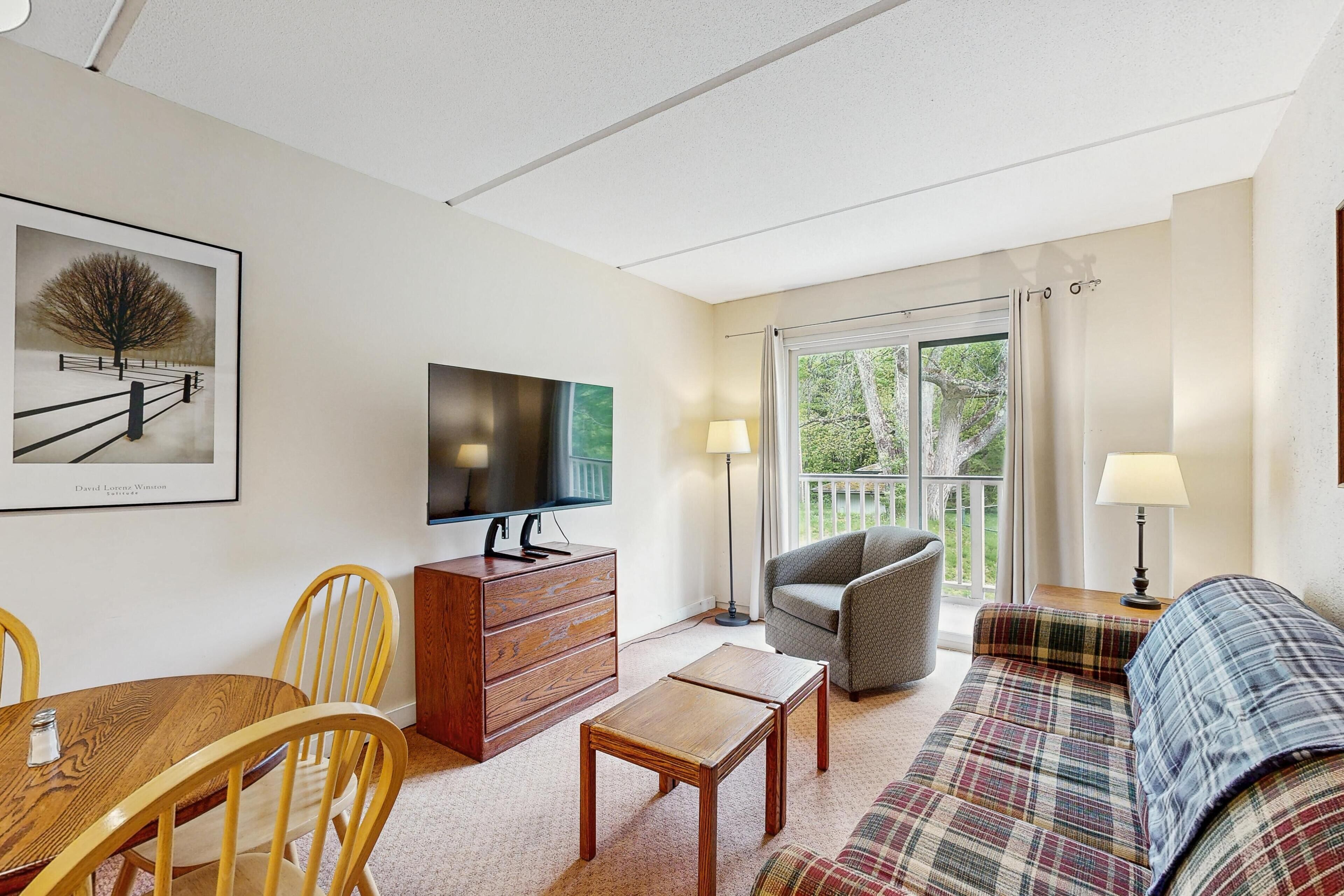 A living room with a TV, wooden furniture, a sofa, and a view through a glass door.