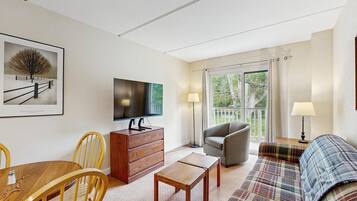 A living room with a TV, wooden furniture, a sofa, and a view through a glass door.