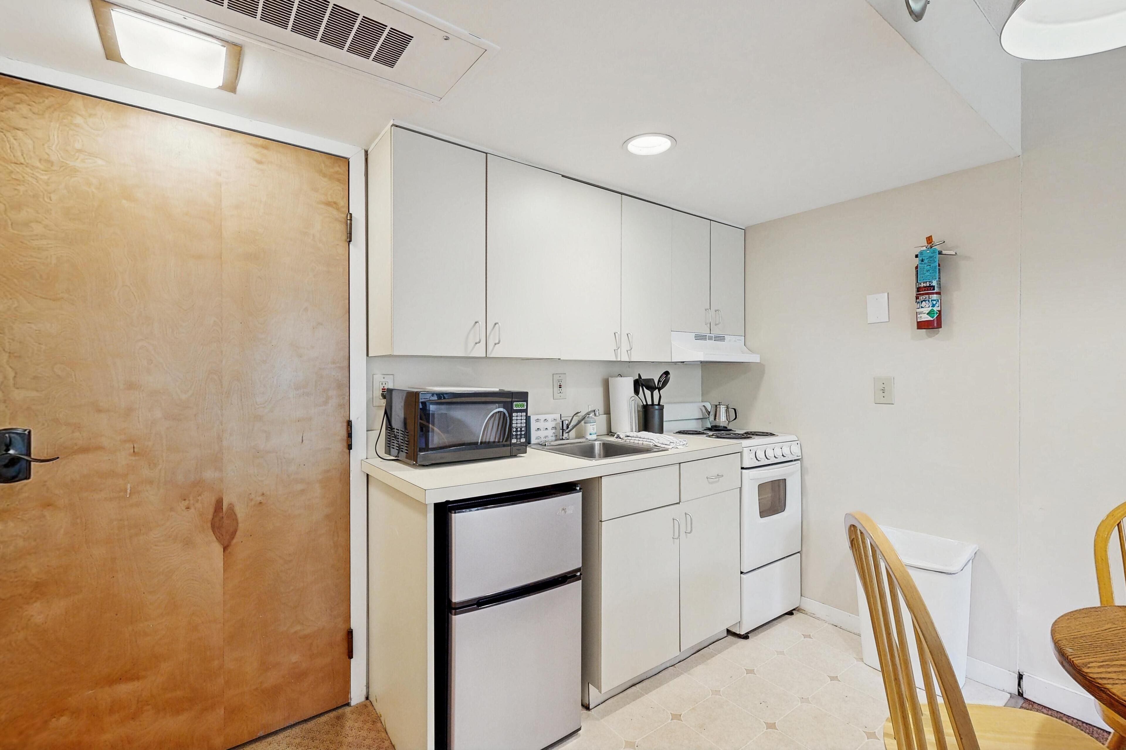 Una cocina compacta con armarios blancos, microondas, fregadero, estufa y refrigerador.