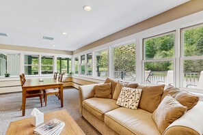 A spacious room with a large window, a beige sofa, a wooden dining table, and a small coffee table. - Four Season Condo:  ski, hike, mountain bike & seasonal pool (Warren)