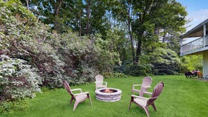 A backyard with a fire pit, three Adirondack chairs, and a motorcycle parked in the background. - Four Season Condo:  ski, hike, mountain bike & seasonal pool (Warren)