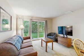 Una sala de estar con un sofá, una mesa de madera, un televisor y una silla.
